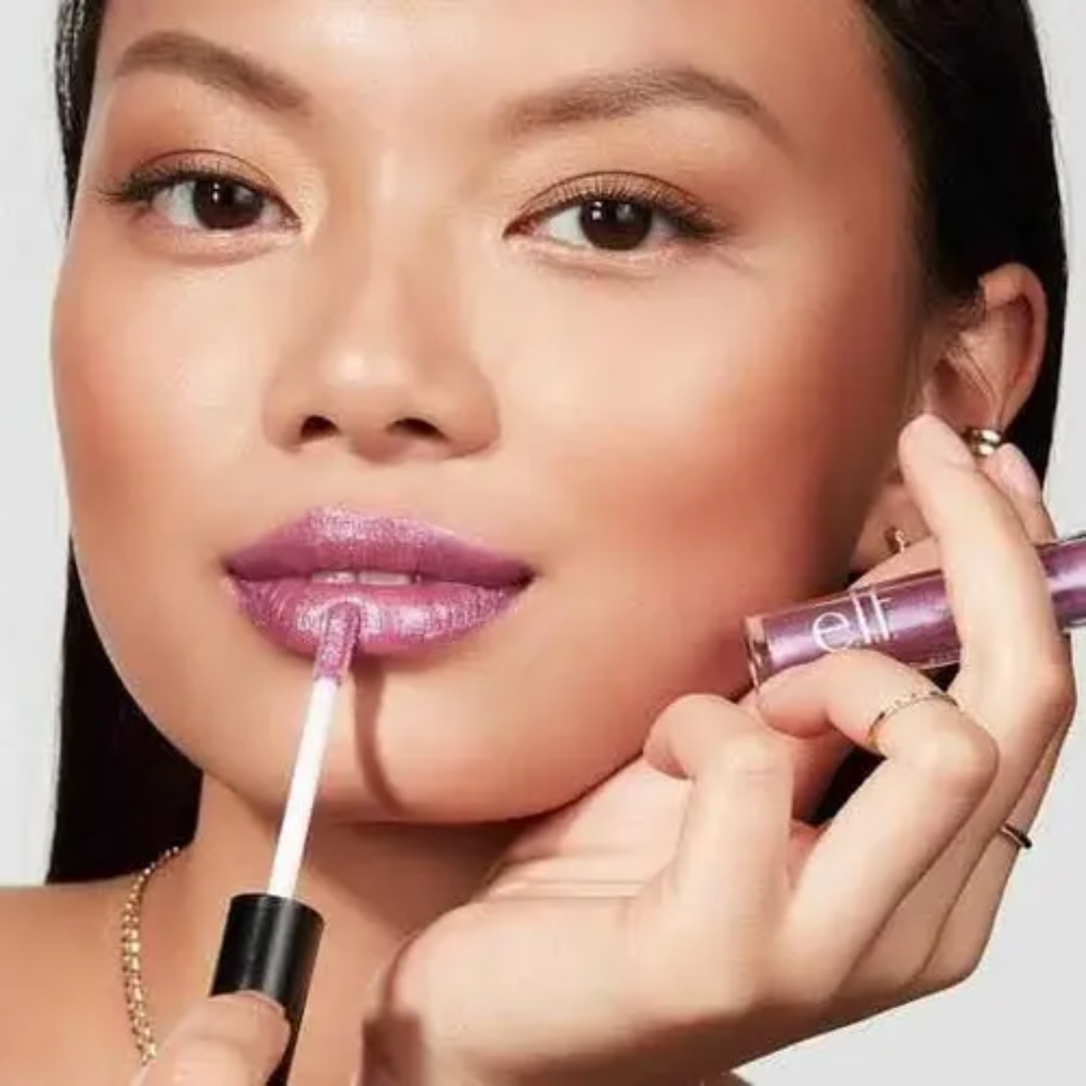 Model brengt e.l.f. Prismatic Lip Gloss Amethyst aan voor een glanzende liplook.